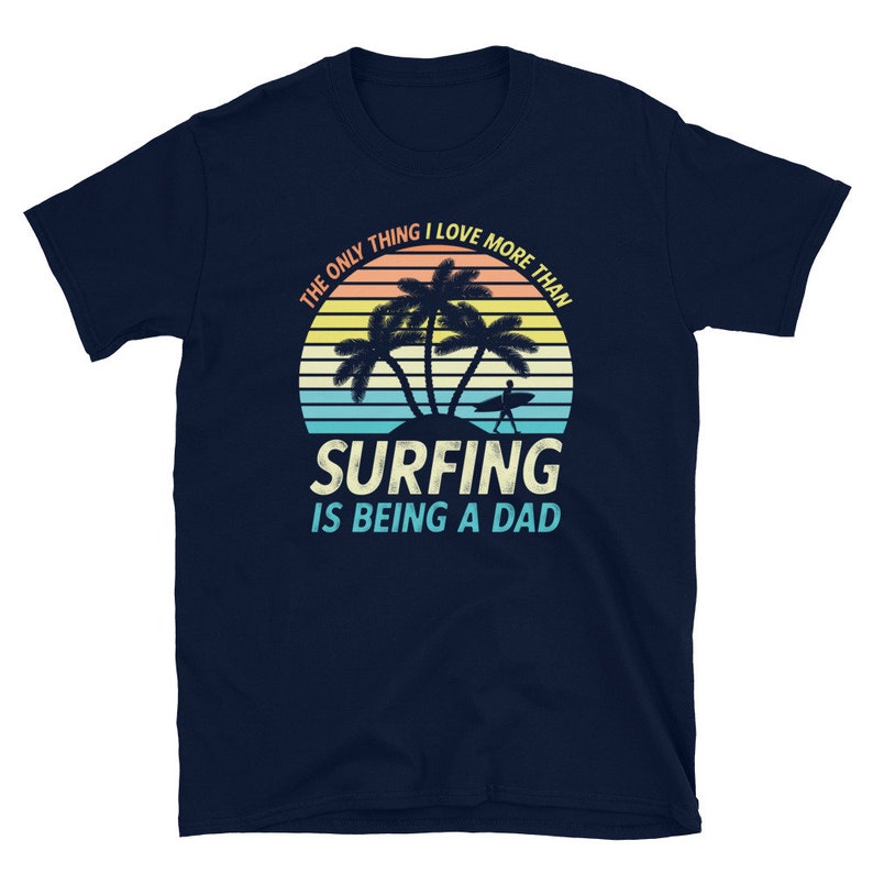 Pu&ograve; includere: T-shirt blu navy con una grafica di tramonto retr&ograve; con palme e un surfista. Il testo recita "L'unica cosa che amo pi&ugrave; del surf &egrave; essere pap&agrave;."