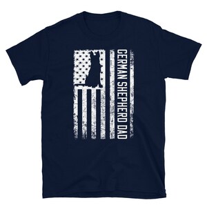 May include: Navy blue t-shirt with a white silhouette of a German Shepherd dog in front of an American flag. The text "GERMAN SHEPHERD DAD" is printed on the right side of the flag.