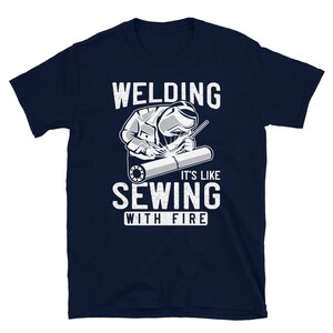 May include: A navy blue t-shirt with a white graphic of a welder working on a pipe. The text "Welding it's like sewing with fire" is printed on the shirt.