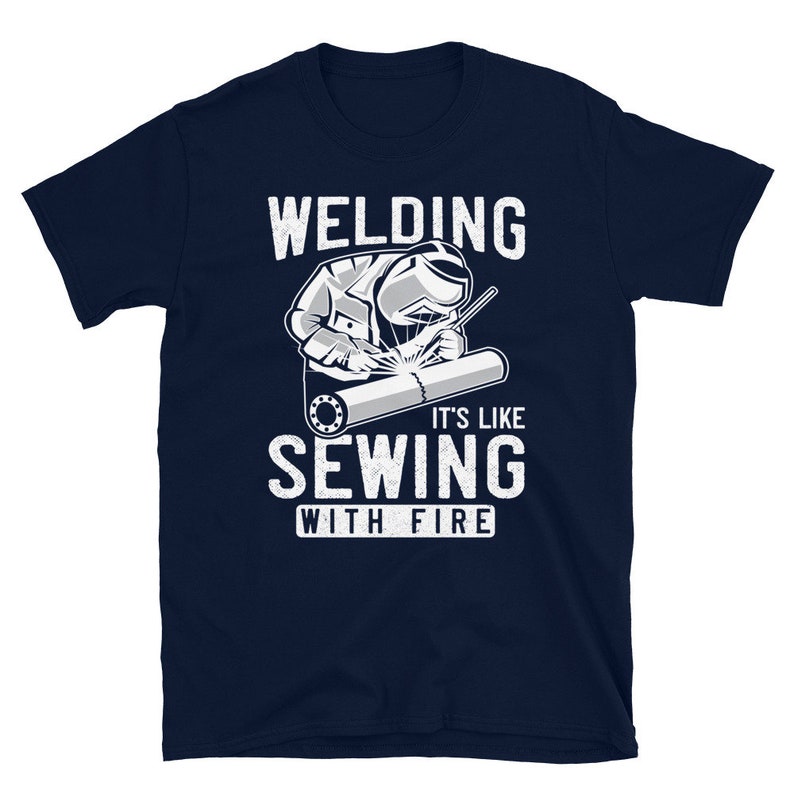 May include: A navy blue t-shirt with a white graphic of a welder working on a pipe. The text "Welding it's like sewing with fire" is printed on the shirt.