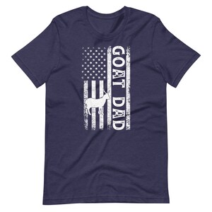 以下が含まれることがあります： アメリカ国旗のデザインが施されたネイビーブルーのTシャツ。旗には白いヤギのシルエットと白い文字で「GOAT DAD」と書かれています。