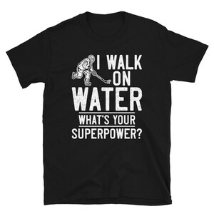 May include: Black t-shirt with white text that reads "I walk on water. What's your superpower?" and a graphic of a hockey player skating on water.