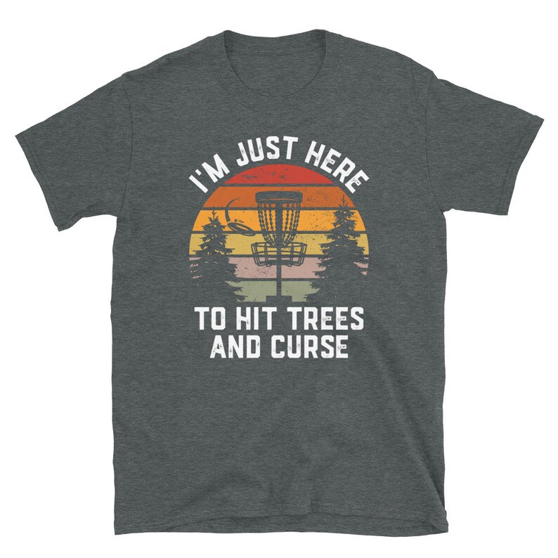 May include: A dark heather grey t-shirt with a vintage-style graphic of a disc golf basket in front of a sunset. The text "I'm Just Here To Hit Trees And Curse" is printed in white below the graphic.