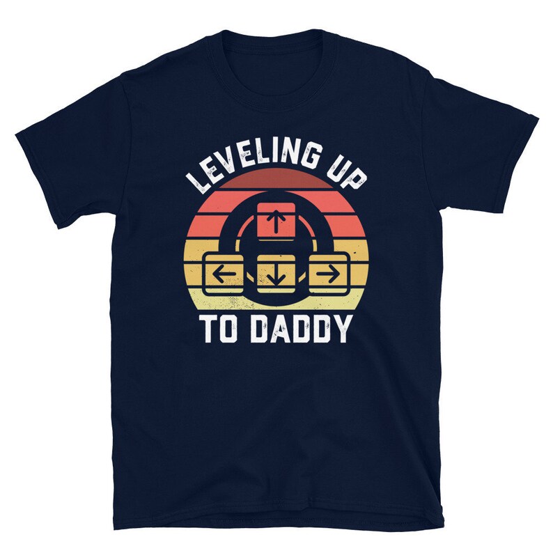 May include: Navy blue t-shirt with a retro-style graphic of a video game controller and the text "Leveling Up To Daddy".