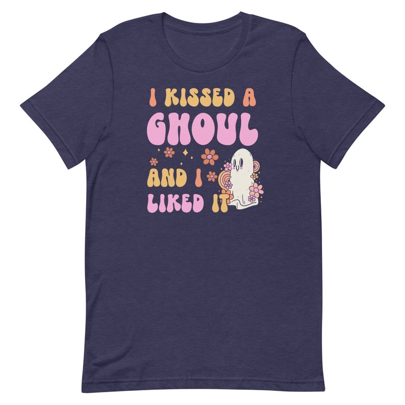 Op de afbeelding: Een marineblauw T-shirt met een roze en oranje afbeelding waarop staat "I kissed a ghoul and I liked it". De afbeelding toont een spook met een roze bloem erachter.