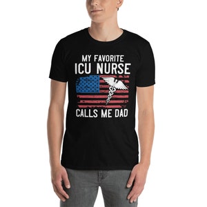 May include: Black t-shirt with a white graphic of an American flag with a medical caduceus symbol and the text "My Favorite ICU Nurse Calls Me Dad".