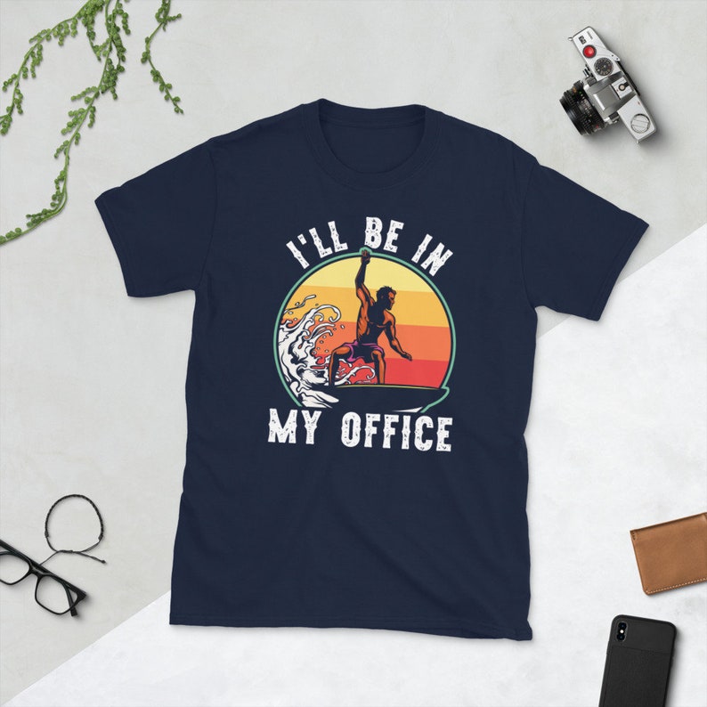 May include: Navy blue t-shirt with a retro-style graphic of a surfer on a wave. The graphic includes the text "I'll be in my office".
