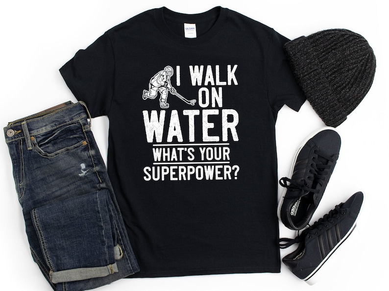 May include: Black t-shirt with a white graphic of a hockey player skating on water. The text "I walk on water. What's your superpower?" is printed on the shirt.