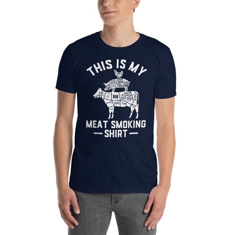 May include: A navy blue t-shirt with a white graphic of a cow, pig, and chicken stacked on top of each other. The graphic is a diagram of the different cuts of meat on each animal. The text "This is my Meat Smoking Shirt" is printed below the graphic.
