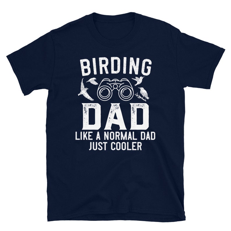 Op de afbeelding: Donkerblauw T-shirt met witte tekst die "Birding Dad Like a Normal Dad Just Cooler" luidt. Het shirt heeft een verrekijker en een vogel illustratie.