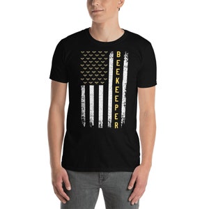 Pode incluir: Camiseta preta com um design de bandeira americana branca e amarela. A bandeira tem um visual desgastado e a palavra "BEEKEEPER" est&aacute; escrita verticalmente do lado direito da bandeira.