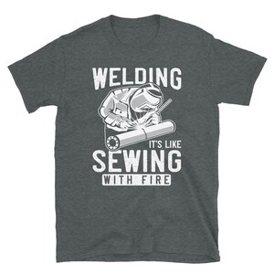 May include: A dark gray t-shirt with a white graphic of a welder and the text "Welding It's Like Sewing With Fire".