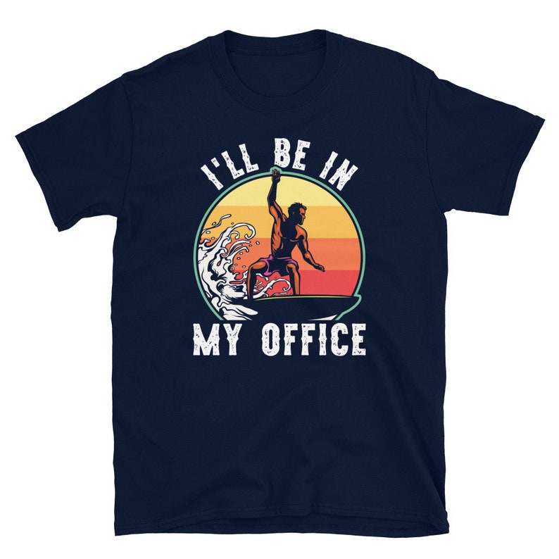 May include: A navy blue t-shirt with a retro-style graphic of a surfer riding a wave. The text "I'll be in my office" is printed in white on the shirt.