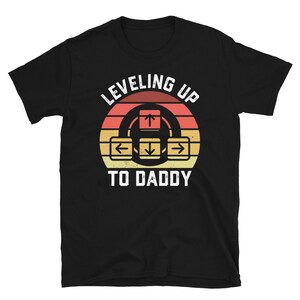 May include: Black t-shirt with a retro-style graphic that says "Leveling Up To Daddy" with an arrow key design.