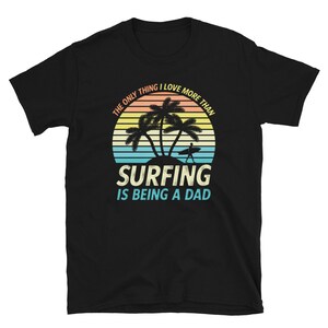 Pu&ograve; includere: Maglietta nera con una grafica di tramonto retr&ograve; e il testo "L'unica cosa che amo pi&ugrave; del surf &egrave; essere pap&agrave;."