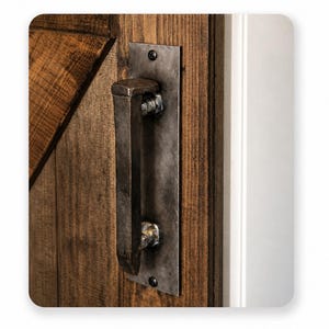 May include: Close-up of a rustic wooden door with a dark metal handle. The door is made of vertical wooden planks with a diagonal design element. The handle is attached to a metal plate with visible screws.