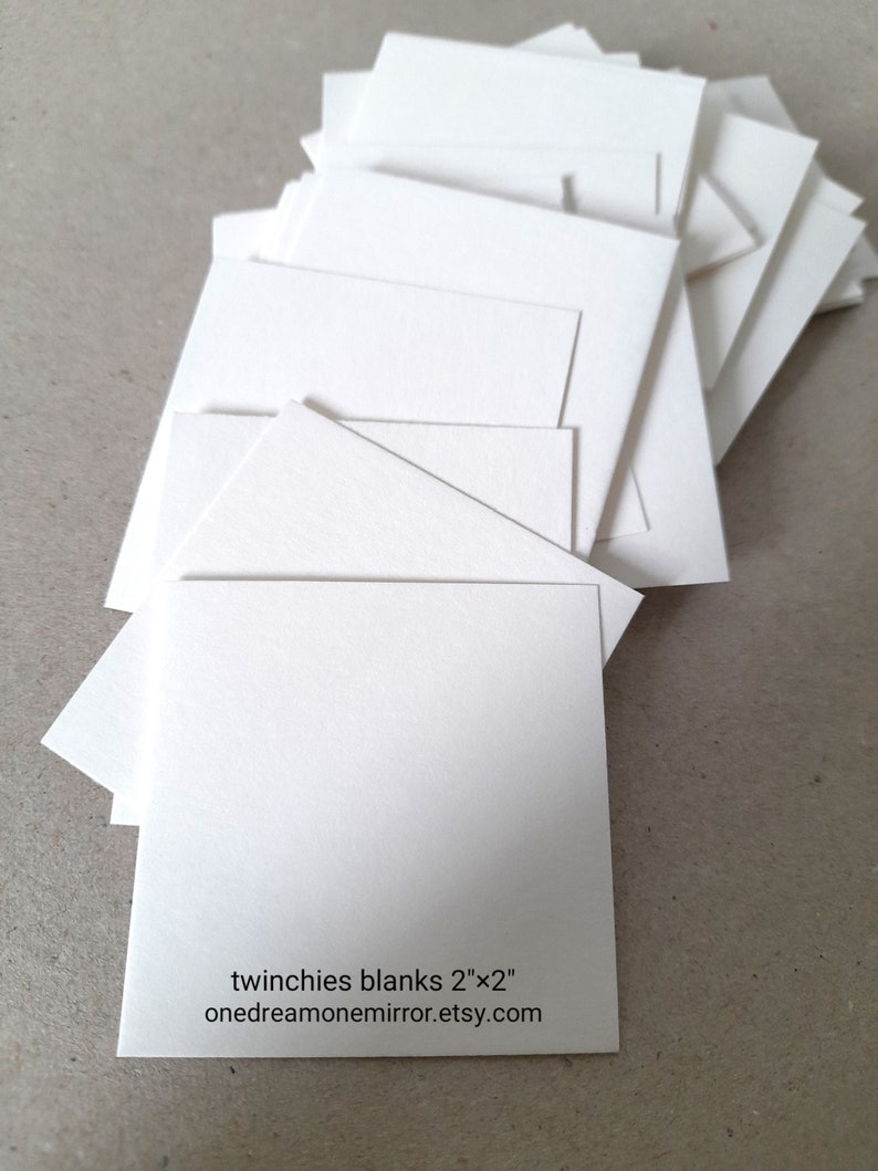 May include: A stack of blank, white square cards, each measuring 2" x 2". The cards are arranged in a slightly fanned-out pattern. Text on one card reads "twinchies blanks 2"x2" onedreamonemirror.etsy.com".