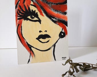 May include: An original painting of a woman's face with red hair and black accents. The artwork features bold brushstrokes, a light skin tone, and a black earring. The artist's signature, "Rachel Leid," and the year 2020 are visible.