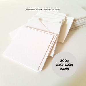 May include: A stack of square, white watercolor paper sheets. The paper is 300g and appears to have a textured surface. The Etsy shop URL is visible at the top. The paper is arranged in a neat pile, ready for use.