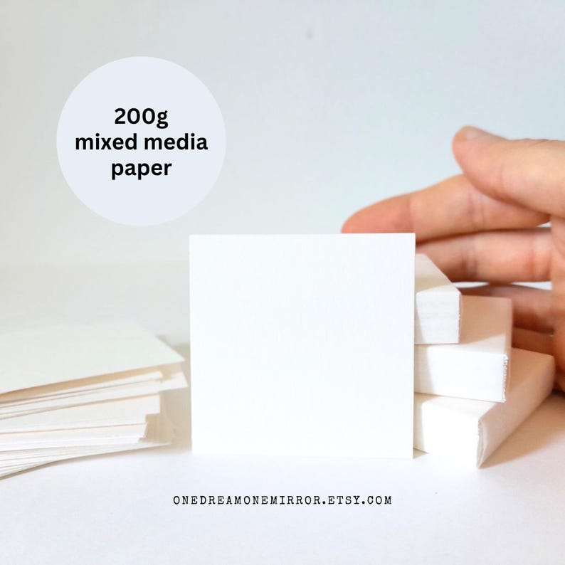May include: Stacks of white mixed media paper, 200g, are displayed. A hand is partially visible, holding a portion of the paper. The paper is square-shaped and appears to be new. The Etsy shop URL is visible at the bottom.