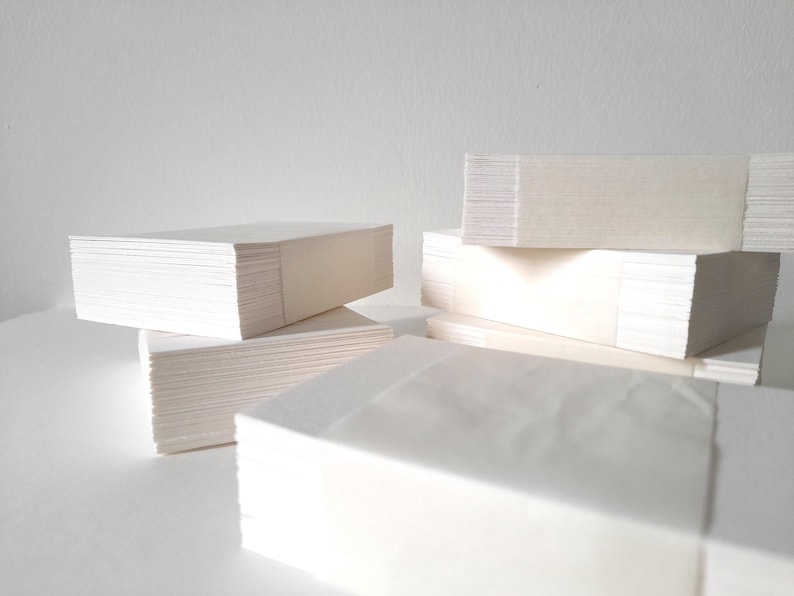 K&ouml;nnte beinhalten: Mehrere Stapel wei&szlig;es Papier, ordentlich angeordnet. Das Papier scheint rechteckig zu sein und wird von einem hellfarbigen Band zusammengehalten. Die Stapel befinden sich auf einer wei&szlig;en Oberfl&auml;che mit wei&szlig;em Hintergrund.
