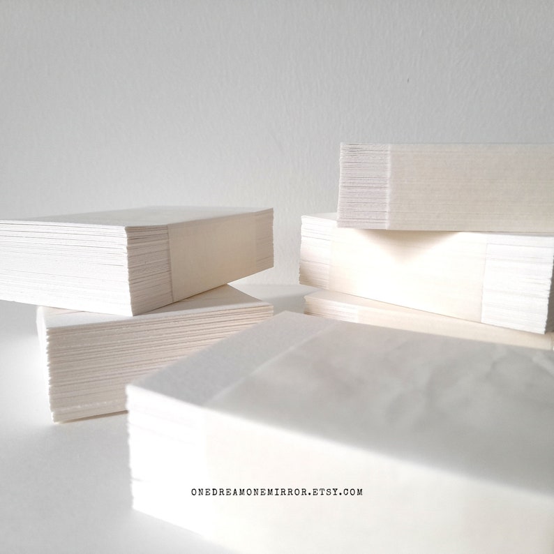 May include: Several stacks of white paper, possibly stationery or notecards, are arranged against a white background. The paper appears to be rectangular and neatly stacked. The image is well-lit, highlighting the texture and edges of the paper.