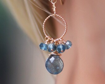 May include: Gold wire earrings with a teardrop-shaped blue gemstone and smaller blue gemstones clustered around the top of the teardrop.