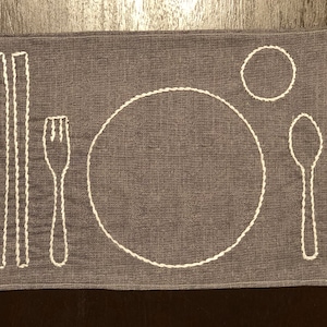 May include: A gray placemat with white embroidered designs of a plate, fork, spoon, and chopsticks.