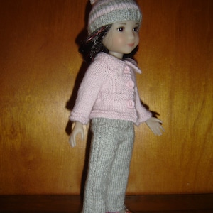 Peut inclure: Une poupée portant un bonnet tricoté gris et rose avec un pompon, un cardigan tricoté rose, un pantalon tricoté gris et des chaussures roses.
