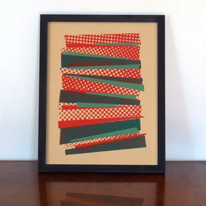May include: Abstract art print in a black frame. The artwork features overlapping strips in red, teal, and cream with polka dot patterns. The background is a light tan color. The framed art is displayed on a dark wood surface.