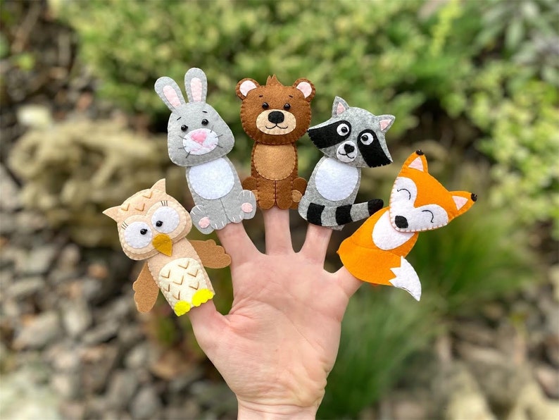 May include: Set of five felt finger puppets featuring woodland animals: an owl, a rabbit, a bear, a raccoon, and a fox. The puppets are all brown, gray, white, and orange.