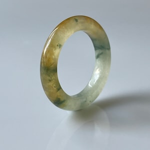 May include: A jade ring with a green and yellow color pattern. The ring is made of a smooth, polished stone.