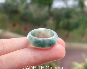 May include: A jade ring with a marbled appearance, featuring shades of green and white. The ring is smooth and polished, with the text "JADEITE Galleria" at the bottom. This ring is a piece of jewelry.