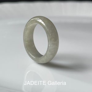 Könnte beinhalten: Ein hellgrüner Jade-Ring mit glatter, polierter Oberfläche. Der Ring ist ein massives Band, das die natürlichen Farbvariationen des Jades zeigt. Der Text "JADEITE Galleria" befindet sich am unteren Bildrand.