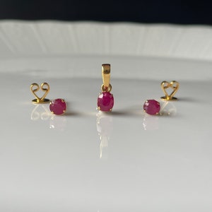 May include: A set of ruby earrings and a pendant necklace. The earrings and pendant feature oval-shaped red gemstones set in gold.