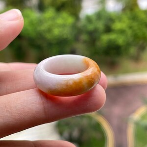 以下が含まれることがあります： 石で作られた滑らかで磨かれたバンドリング。片側は淡い半透明の白、もう片側は温かみのある鮮やかなオレンジイエローへと変化するグラデーションカラーが特徴で、丸みを帯びた厚みのあるプロファイルと光沢のある仕上げが施されています。