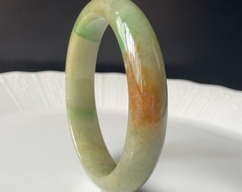 May include: A jade bangle bracelet with a green, white, and brown color scheme. The bangle is smooth and polished.