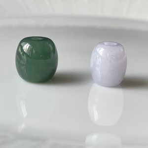 May include: Two round jade beads, one green and one light purple, on a white surface.