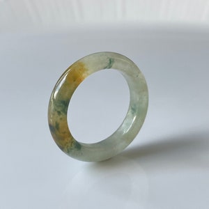 May include: A green, white, and yellow jade ring. The ring is made of a smooth, polished stone and has a simple, elegant design.