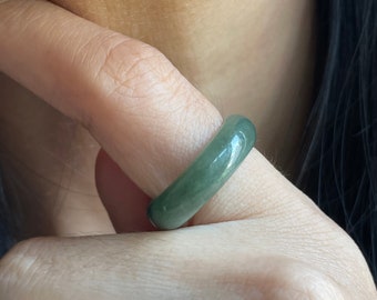 May include: A green jade ring with a smooth, polished finish. The ring is worn on a finger.
