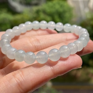 Pode incluir: Um bracelete de jadeíta azul claro com contas redondas. O bracelete é feito de jadeíta natural e é um belo exemplo desta pedra preciosa.