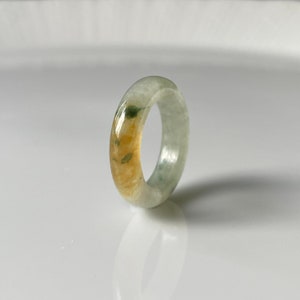 Puede incluir: Un anillo de jade de color verde claro y amarillo. El anillo está hecho de una piedra lisa y pulida.