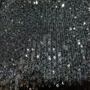 Può includere: Tessuto nero con paillettes argentate. Le paillettes sono piccole e rotonde e sono disposte in uno schema fitto.