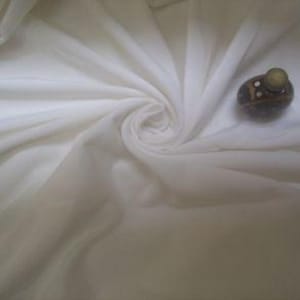 May include: A close-up of white, translucent fabric arranged in a spiral. A small, decorative stone object with a light green top and small white accents rests on the fabric, providing a contrast in texture and colour.