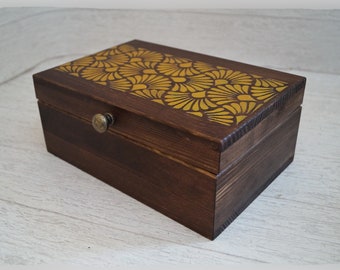 May include: A wooden box with a hinged lid and a brass knob. The top of the box is decorated with a yellow geometric pattern.