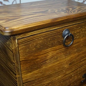 Puede incluir: Un cofre de madera con un acabado marr&oacute;n c&aacute;lido. El cofre presenta un tirador de anillo y veta de madera visible. El dise&ntilde;o es simple y cl&aacute;sico, adecuado para almacenamiento o como pieza decorativa. El cofre es rectangular con una parte superior ligeramente curvada.