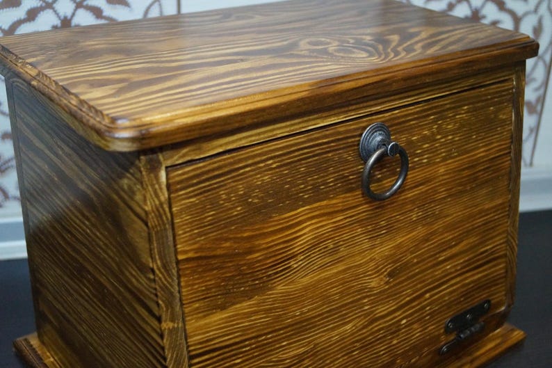 Puede incluir: Un cofre de madera con un acabado marr&oacute;n c&aacute;lido. El cofre presenta un tirador de anillo y veta de madera visible. El dise&ntilde;o es simple y cl&aacute;sico, adecuado para almacenamiento o como pieza decorativa. El cofre es rectangular con una parte superior ligeramente curvada.