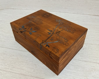 May include: A wooden box with a floral design. The box is stained a dark brown color and has a blue floral pattern on the top and sides. The box has a hinged lid and is made of natural wood.