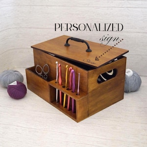May include: A wooden craft storage box with a handle, open lid, and compartments for tools. The box is stained a warm brown and includes the text "PERSONALIZED sign". Yarn balls and scissors are also visible.