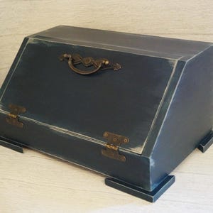 Puede incluir: Una caja de madera azul marino con tapa inclinada, bisagras de lat&oacute;n y un asa decorativa. La caja tiene un acabado envejecido, lo que le da un aspecto vintage. La caja es rectangular y se apoya sobre cuatro peque&ntilde;os pies.